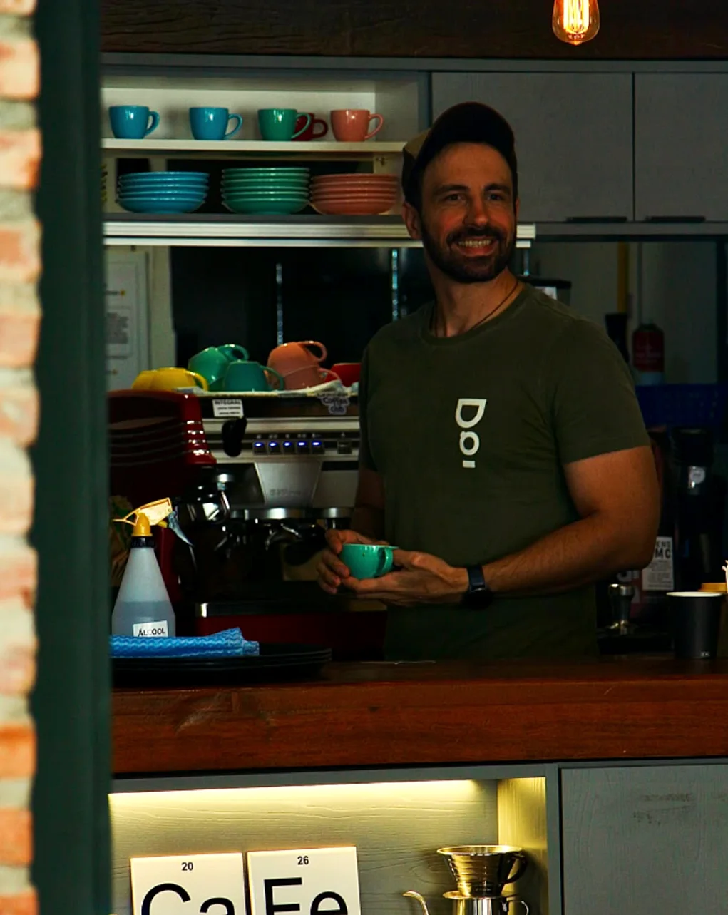 Barista sorrindo com uma xícara verde atrás do balcão