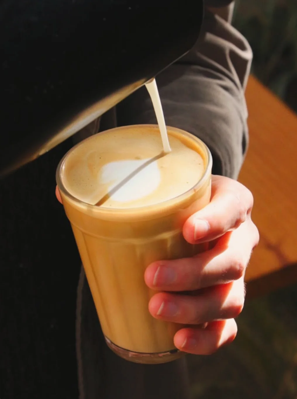 Leite sendo vertido num latte em copo de vidro